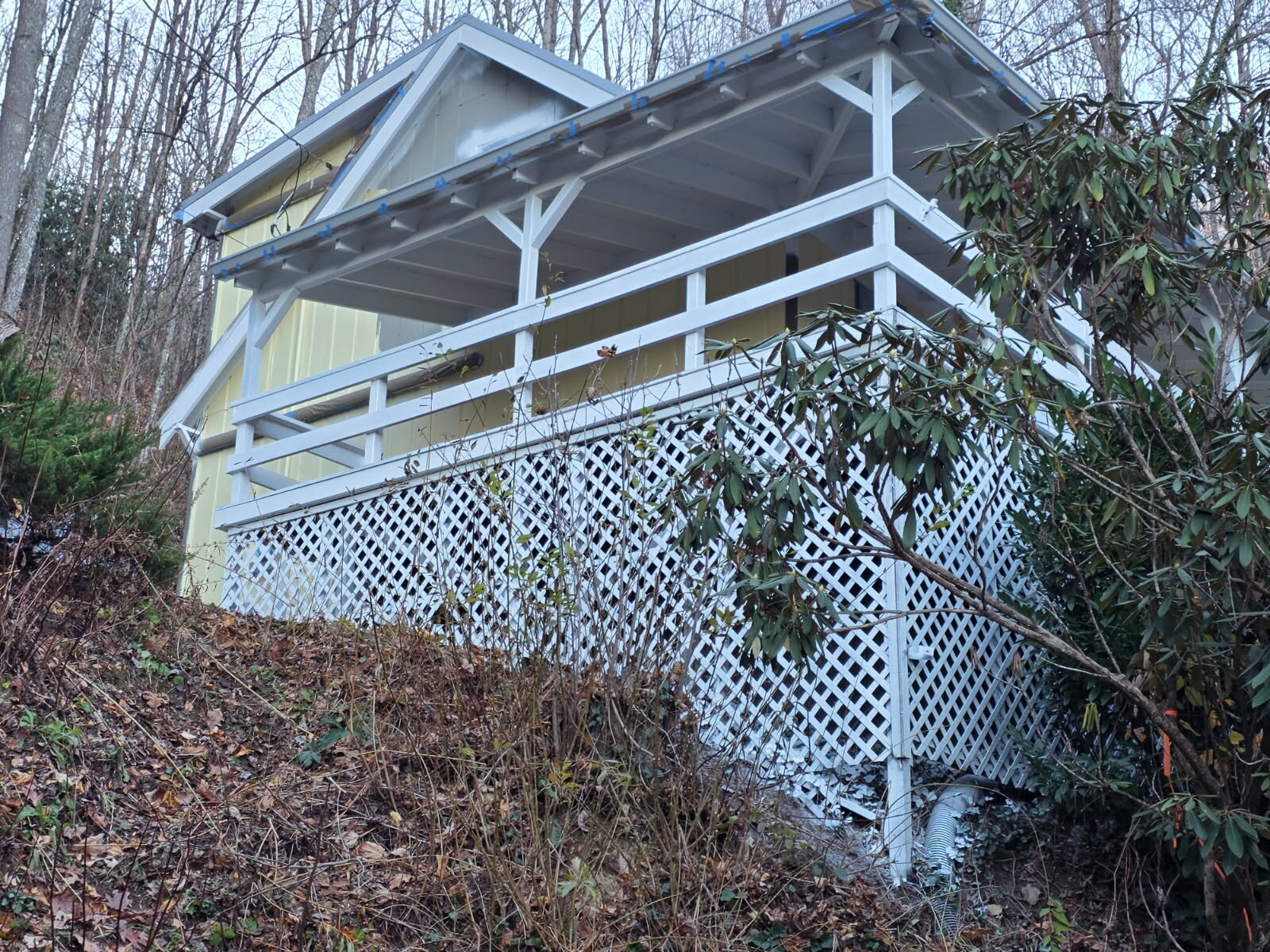 Sage-yellow mountain cabin with white-lattice deck above hillside