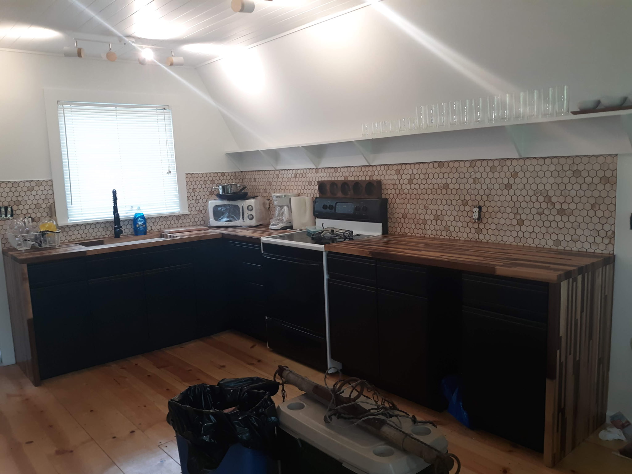 Full kitchen renovation by Flying Colors — black cabinet refinish, butcher block counters, hex tile backsplash, tongue-and-groove ceiling